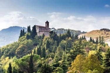 Eine Landschaft mit einem historischen Kloster, das auf einem bewaldeten Hügel thront.