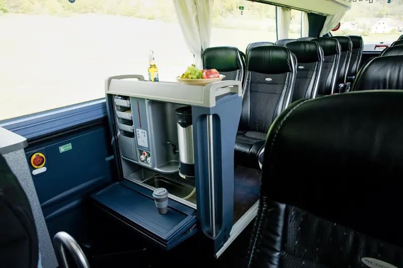 Innenansicht eines komfortablen Reisebusses mit Sitzen und einem Getränkehalter und Kaffeemaschine.