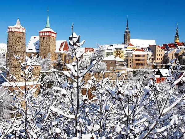 Die Altstadt mit Stadtmauer von Bautzen an einem sonnigen Wintertag mit schneebedeckten Dächern und Bäumen.