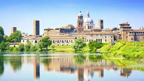 Historische Altstadt von Mantua mit dem Palazzo Ducale, die sich an einem sonnigen Tag im ruhigen Fluss Mincio spiegelt, ein Highlight jeder Studiosus Gruppenreise nach Italien.