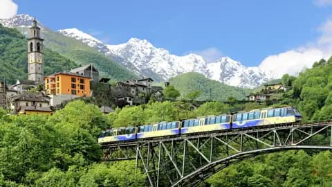 Die Centovalli-Bahn fährt auf einer Studienreise im Tessin über ein Viadukt bei Intragna vor einer Kulisse aus schneebedeckten Alpen.