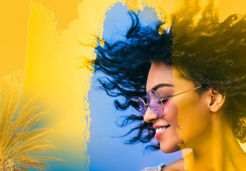 Eine Frau mit lockigem Haar und Sonnenbrille vor einem bunten Hintergrund.
