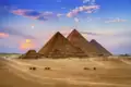 Die Pyramiden von Gizeh in Ägypten bei Sonnenuntergang mit Kamelen im Vordergrund.