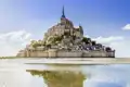 Mont Saint-Michel bei Ebbe, mit sichtbarem Sandstrand und Spiegelung im Wasser