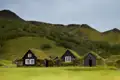 Traditionelle isländische Häuser aus Steinmauern mit begrünten Dächern in einer grünen Hügellandschaft.