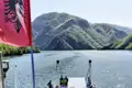 Bootstour auf einem See in Albanien mit Blick auf die bewaldeten Hügel. Die albanische Flagge ist im Vordergrund sichtbar.