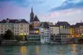 Auf unserer Gruppenreise mit Studiosus genießen wir den Blick auf die Altstadt von Basel mit der Martinskirche und der Mittleren Brücke, beleuchtet am Rheinufer bei Dämmerung.