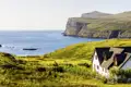 Auf unserer Gruppenreise mit Studiosus genießen wir den Ausblick auf ein typisches Haus an der Küste der Isle of Skye,  umgeben von grünen Hügeln und dem Meer. Ein Natur Highlight auf unserer Kreuzfahrt durch Schottland.