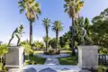 Bronzestatuen im sonnigen Schlossgarten von Sisis Achilleion-Palast auf Korfu, umgeben von hohen Palmen und grünen Pflanzen, ein Highlight unserer Studiosus Gruppenreise.