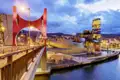 Blick von der roten La Salve Brücke auf das beleuchtete Guggenheim-Museum in Bilbao am Fluss Nervión in der Abenddämmerung, ein toller Ausblick, den wir auf unserer Gruppenreise mit Studiosus genießen.