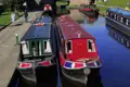 Farbenfrohe Narrowboats liegen auf dem Llangollen-Kanal in Wales. Im Hintergrund eine alte Steinbrücke und Spaziergänger am Ufer, ein Highlight unserer Rundreise mit Studiosus.