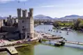 Luftaufnahme des UNESCO-Welterbes Caernarfon Castle am Hafen von Caernarfon mit Segelbooten vor walisischer Bergkulisse, ein Highlight unserer Gruppenreise mit Studiosus