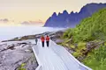 Ein Paar in roten Jacken auf einem Holzsteg an der Felsküste von Senja, im Hintergrund die Okshornan-Gipfel, ein tolles Naturhighlight auf userer Gruppenreise mit Studiosus.