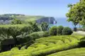 Kunstvoll geschnittene Hecken im Garten von Étretat mit Blick auf die berühmte Felsformation Porte d'Aval an der Küste der Normandie, welche wir bei unserer Rundreise mit Studiosus bewundern können.