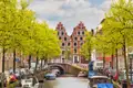 Auf unserer Rundreise mit Studiosus bewundern wir malerische Gracht in Haarlem mit Booten am Ufer, Bäumen mit frischem Laub und traditionellen niederländischen Giebelhäusern.