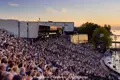 Die vollbesetzte Tribüne der Seebühne der Bregenzer Festspiele am Bodensee während des Sonnenuntergangs vor einer Vorstellung, ein Highlight unserer Eventreise.