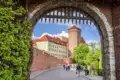 Eine Reisegruppe spaziert auf einer gepflasterten Straße durch ein historisches Burgtor zum Wawelschloss in Krakau, ein toller Anblick auf unserer Gruppenreise mit Studiosus nach Polen.
