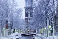 Winterliche Stimmung in Amsterdam: Eine schneebedeckte Gracht mit beleuchteten Laternen und Blick auf den Munttoren, ein toller Anblick auf unserer Gruppenreise nach Amsterdam.