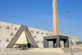 Die moderne Fassade des Grand Egyptian Museum in Gizeh, davor ein hoher, antiker Obelisk unter strahlend blauem Himmel, ein architektonisches Highlight unserer Gruppenreise.