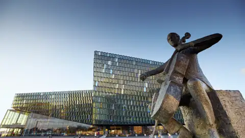 Bronzestatue eines Cellisten vor der beeindruckenden Glasfassade des Konzerthauses Harpa in Reykjavik, ein Highlight jeder Gruppenreise nach Island
