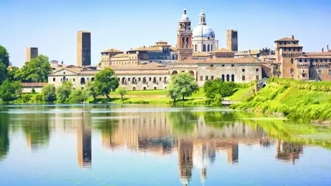 Die historische Altstadt von Mantua mit ihren Palästen und Türmen spiegelt sich an einem Sonnentag im ruhigen Wasser des Mincio, ein Highlight unserer Studiosus Gruppenreise nach Italien.