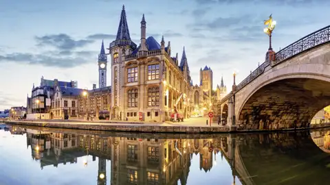 Abenddämmerung in Gent: Die beleuchteten Gildehäuser am Graslei spiegeln sich im Wasser der Leie neben der St.-Michaels-Brücke, ein Highlight unserer Studiosus Gruppenreise nach Belgien.