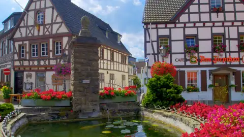 Blumengeschmückter Brunnen im historischen Zentrum von Rhöndorf mit Blick auf traditionelle Fachwerkhäuser sehen wir auf unserer Gruppenreise mit Studiosus.