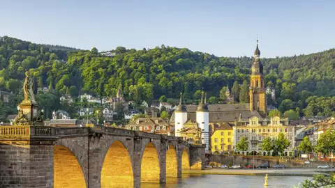 Auf unserer Gruppenreise mit Studiosus bewundern wir die Alte Brücke über den Neckar in Heidelberg, von der Morgensonne beleuchtet, mit der Heiliggeistkirche und der Altstadt.