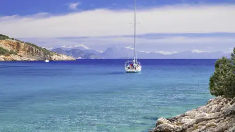 Ein Segelboot ankert in einer idyllischen Bucht vor Ithaka im türkisblauen Ionischen Meer, umgeben von Felsklippen. Ein schönes Fotomotiv auf unserer Eventreise.