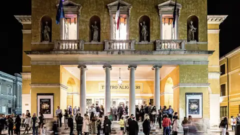 Elegant gekleidete Gäste einer Eventreise versammeln sich vor dem beleuchteten Teatro Alighieri in Ravenna.