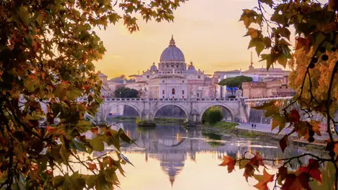 Stimmungsvoller Sonnenuntergang in Rom mit Blick auf den Petersdom, der sich im Tiber spiegelt, umrahmt von Herbstlaub. Ein perfekter Ausblick für unsere Studiosus Eventreise.