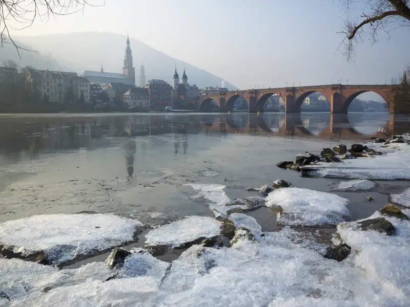 Winterliche Ansicht von Heidelberg mit Eisschollen am Neckarufer und der Alten Brücke vor der nebligen Altstadtkulisse. Ein schönes Fotomotiv während Ihrer Gruppenreise.