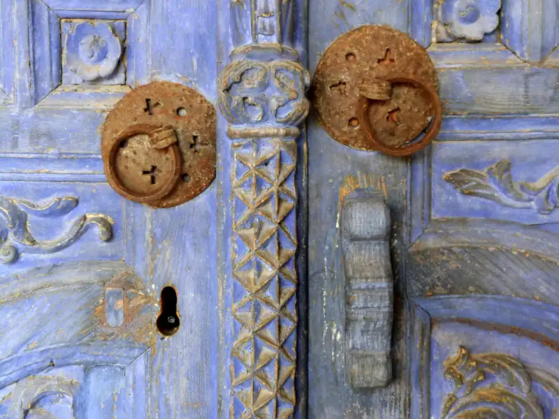 Mit Ihrem Studiosus-Reiseleiter werden Sie bei der Gruppenreise für Singles und Alleinreisende auch auf schöne Details aufmerksam gemacht. Hier eine traditionelle alte, blaue Holztür mit verrosteten Metallringen und verzierten Schnitzereien.
