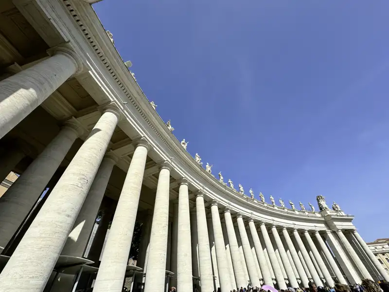 Imposanter Eindruck in Rom während unserer Singlereise in die Ewige Stadt: die Kolonnade der Peterskirche mit ihren zahlreichen Säulen und Statuen vor blauem Himmel.