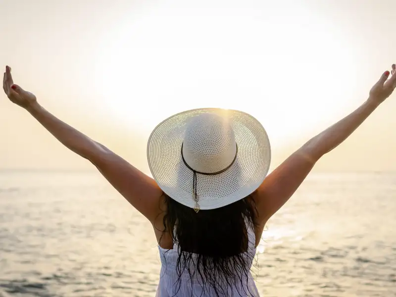 Frau mit Sonnenhut genießt den Sonnenuntergang am Meer.