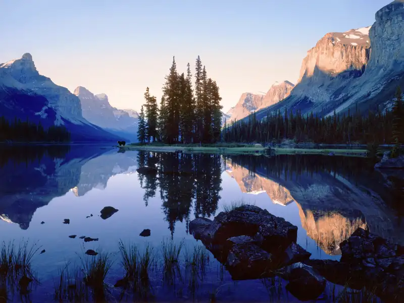 Auf unserer Studienreise durch Kanada gleiten wir mit einem Ausflugsboot über den Maligne Lake, der fotogen zwischen Schneegipfeln schimmert. Die schroffen, felsigen Berge spiegeln sich im glatten Wasser.