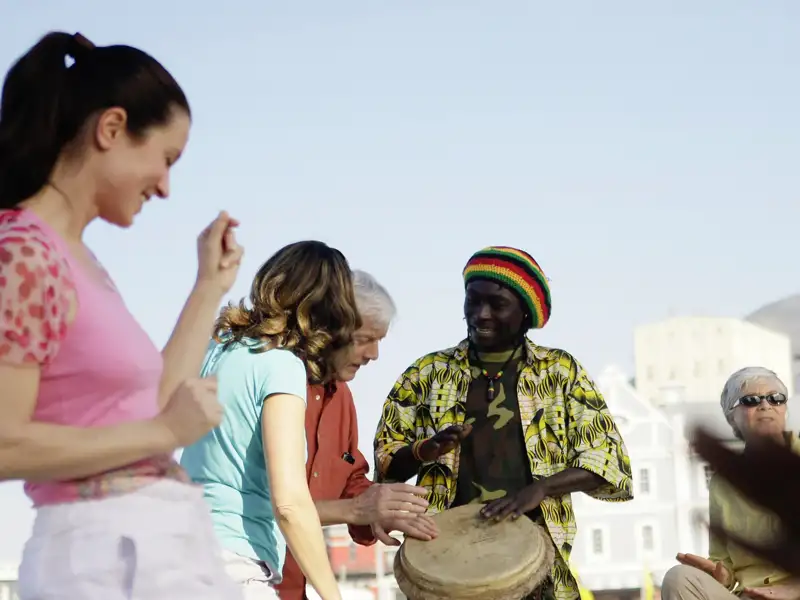 Eine Reisegruppe unterwegs an der Waterfront in Kapstadt trifft auf einen Trommler. Begegnungen wie diese gehören zur DNS einer Studiosus-Reise