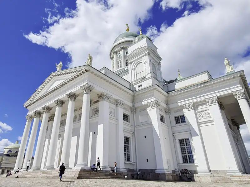 Ein Highlight unserer Studienreise in kleiner Gruppe von Schweden bis Finnland: der Dom von Helsinki, ein imposantes weißes Gebäude mit Säulen und einer grünen Kuppel, unter einem strahlend blauen Himmel.