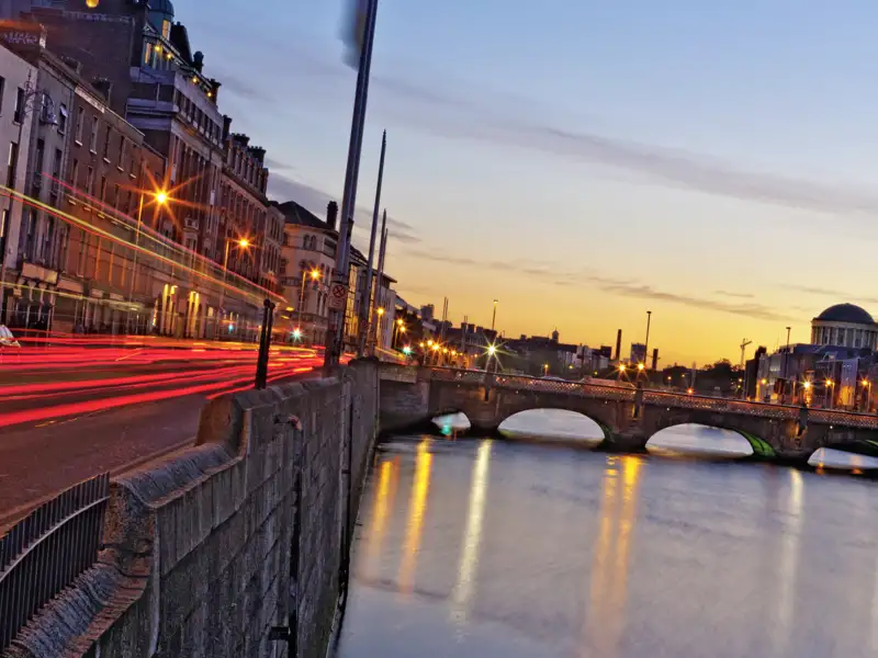 Dublin bei Sonnenuntergang mit Blick auf den Fluss Liffey und die O'Connell Street. Das Bild zeigt die Lichter der Stadt und den Fluss, der im Abendlicht glitzert.