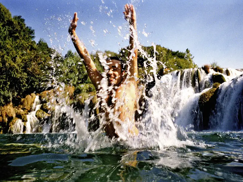 Ein junger Reisender spritzt vergnügt im Wasser der Krka-Wasserfälle, die Sie auf der smart&small-Reise durch Kroatien optional besuchen können.