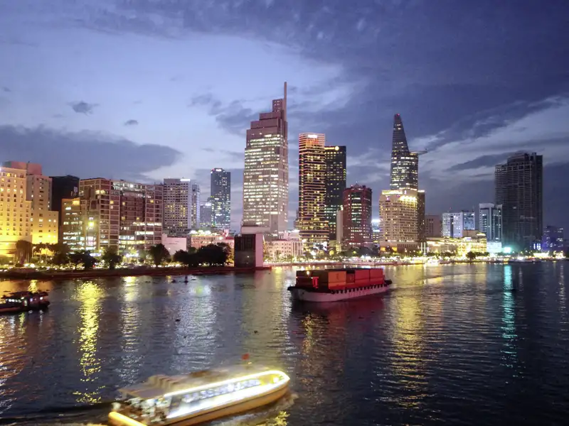 Ein Boot fährt nachts auf dem Saigon-Fluss vor der beleuchteten Skyline