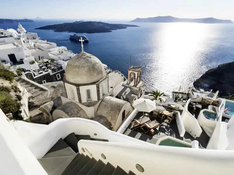 Weiße Gebäude und eine Kuppelkirche auf Santorin mit Blick auf das Meer und ein Kreuzfahrtschiff
