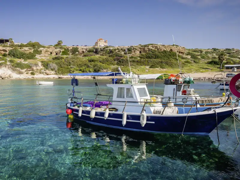 Unsere Reise führt uns auch in den Küstenort Paphos, wo die Cafés am Hafen zu einer Pause einladen und wir Fischerboote, die im glasklaren Wasser ankern, beobachten können.