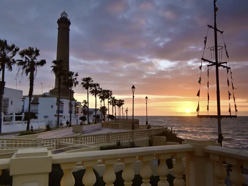 Sonnenuntergang an einem Leuchtturm mit Palmen und einer Promenade