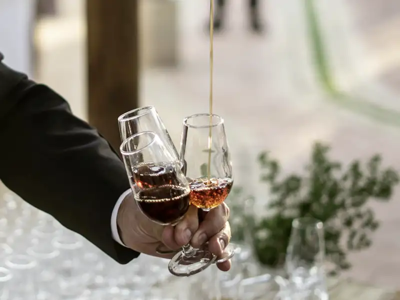 Eine Hand hält drei Sherrygläser, in eines davon wird gerade eingeschenkt.