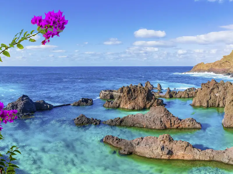 Die natürlichen Meeresschwimmbecken von Porto Moniz auf Madeira, ein im Reiseverlauf geplanter Besuch, mit türkisfarbenem Wasser und dunklen Lavafelsen unter blauem Himmel.