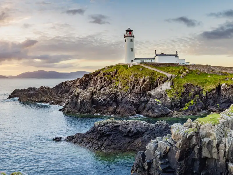 Immer wieder zieht uns auf unserer Rundreise durch Irland die raue Küste in ihren Bann. Noch heute leben Menschen in den oft weit abgelegenen Leuchttürmen. Hier ein Leuchtturm auf felsiger Küste bei Sonnenuntergang.
