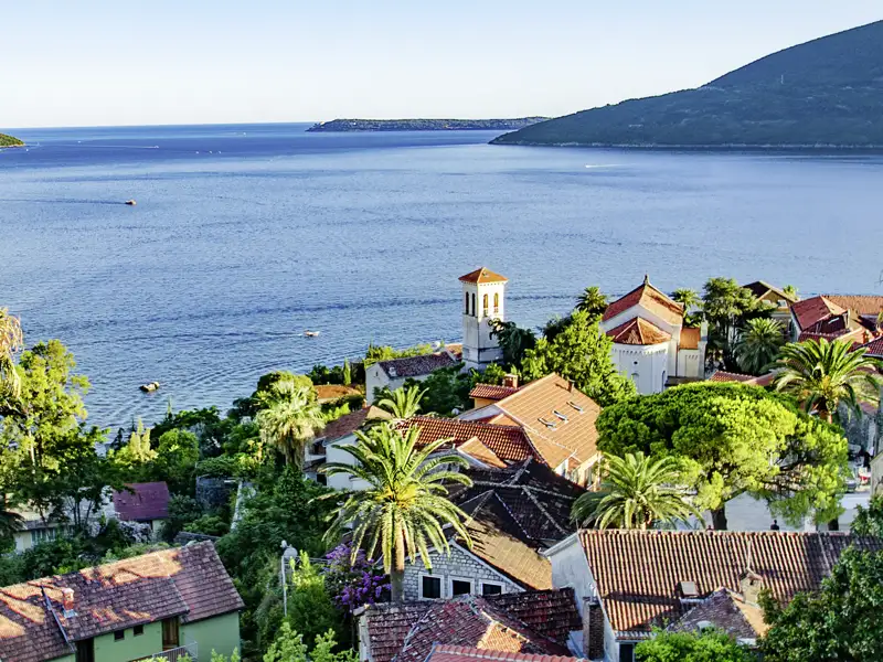 Panoramablick auf eine Küstenstadt mit roten Dächern, Palmen und türkisfarbenem Meer