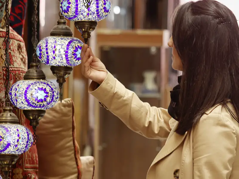 Eine Frau betrachtet handgefertigte Mosaiklampen im Detail.