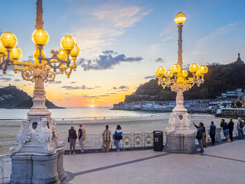 Bestaunen Sie den Sonnenuntergang über der Bucht von La Concha mit Blick auf die Stadt San Sebastián und die beleuchteten Laternen an der Promenade auf Ihrer Studiosus Silvesterreise.